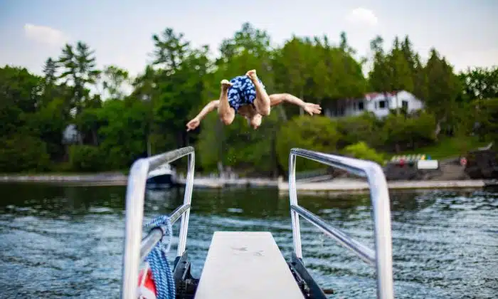 A boy doing a front flip into the lake from a diving board