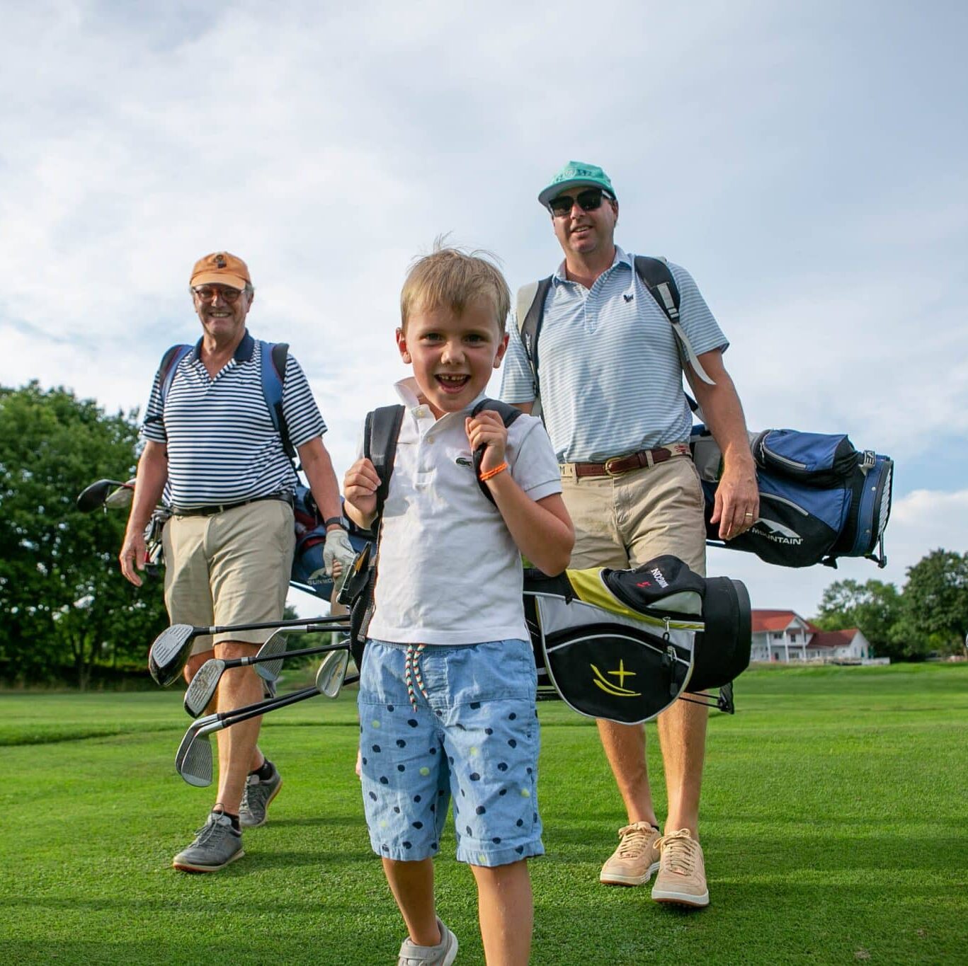 Three generations of golfers walking down fairway with gold bags on shoulders