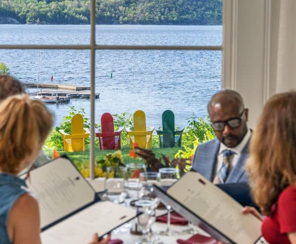 Group eating in Ardelia's restaurant with waterview of the harbor. Iconic colorful adirondack chairs sit outside the window on the lawn.