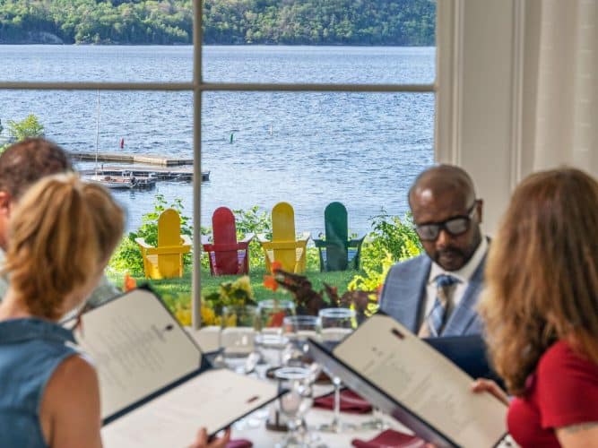 Group eating in Ardelia's restaurant with waterview of the harbor. Iconic colorful adirondack chairs sit outside the window on the lawn.