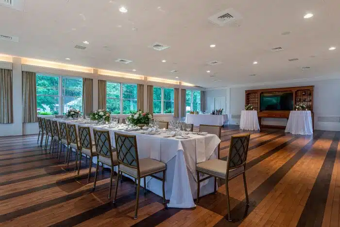 A room set up for an event with family style tables and a bar in the far right corner