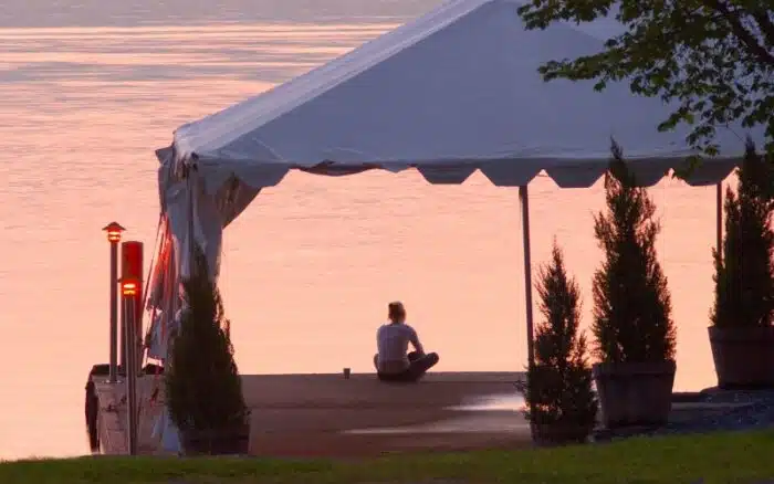 Women sits on the North Dock along reflecting over a pink flowing Lake Champlain