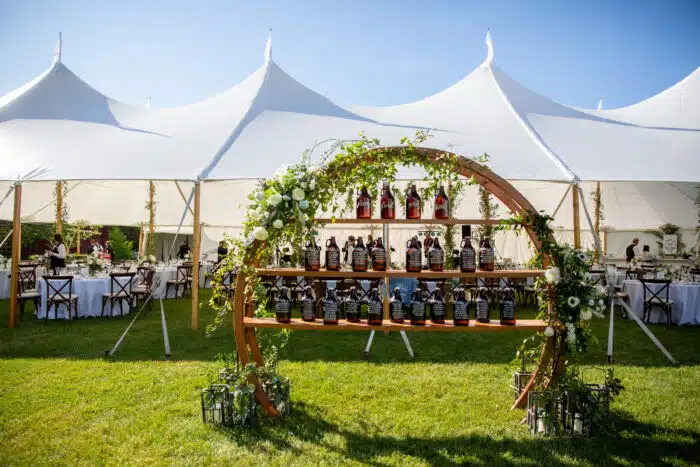 Gatehouse Lawn tented wedding reception with table assignment displayed on growler bottles