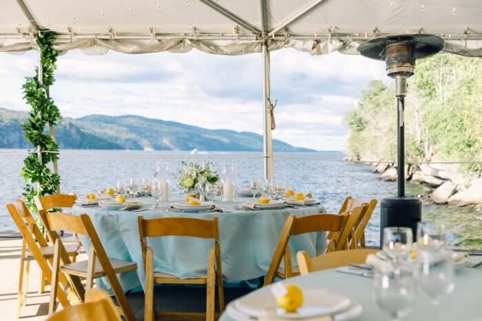 North Dock set for a dinner with light blue tablecloths and lemon place settings, beyond the tent a beautiful view of Lake Champlain and the Adirondacks.
