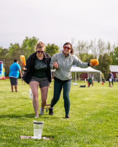 Two women running a three-legged challenge with wet sponges. Team building activity at Basin Harbor