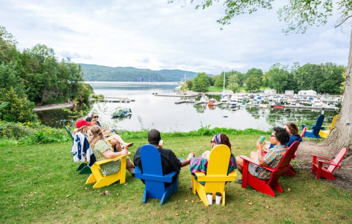 A group of people sitting in Adirondack chairs that overlook the lake.