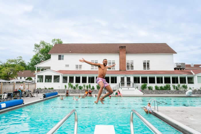 A man jumping off a diving board into the pool backwards, with his arms outstreached.