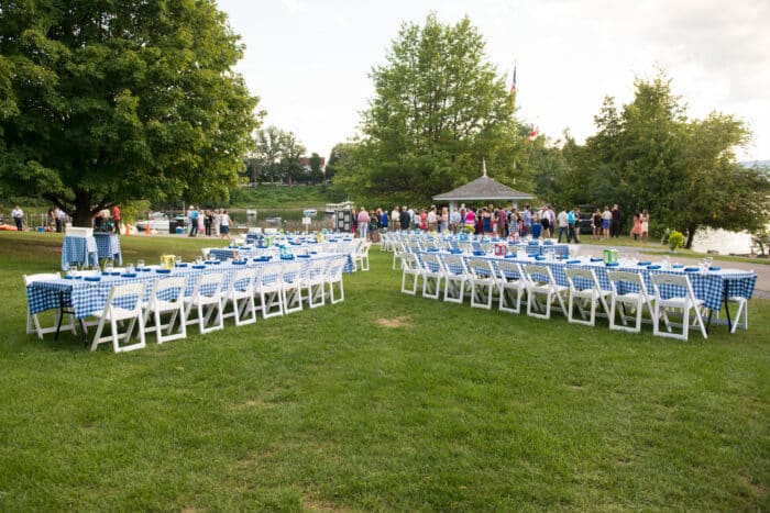 A lawn with several long rectangular tables draped in blue and white table clothes, set up for an event.