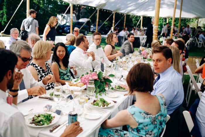 A group of people sitting at a table under a wedding tent talking with on another.
