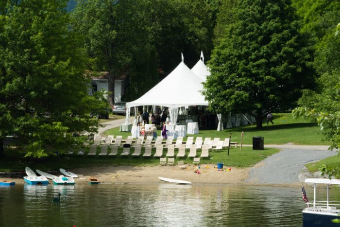 A view from the lake of a tent set up near the beach for a wedding.