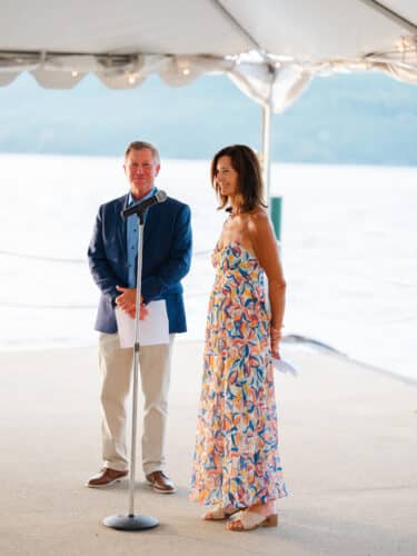 A woman giving a speech under the North Dock tent while a man stands to her right.