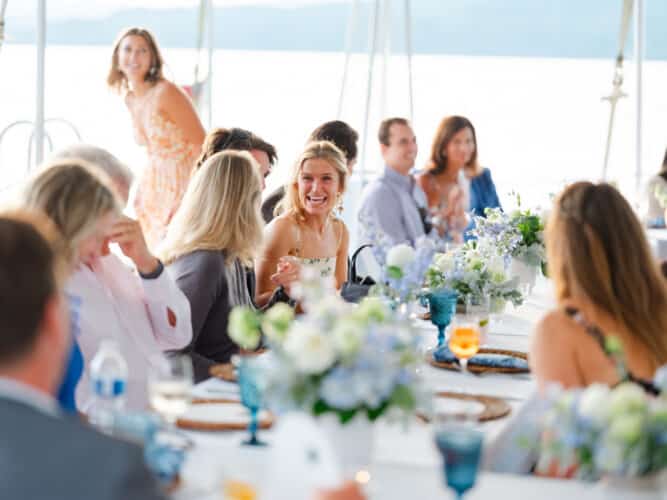 A group of people dining at a rectangular table set at the North Dock for the special event. The table has blue and white flower arrangements for the centerpieces.