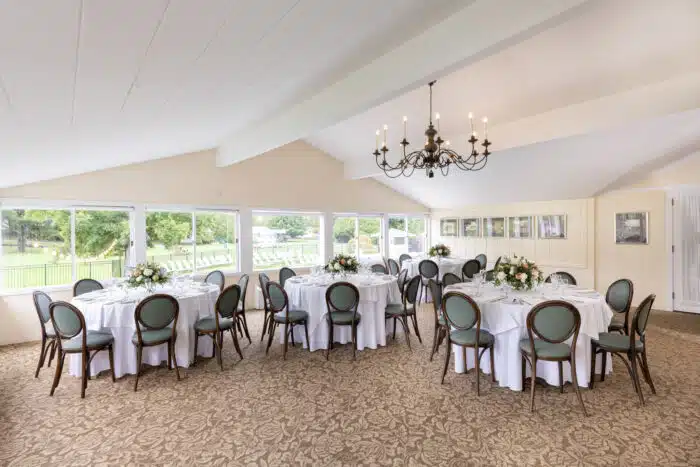 Several round tables with white table clothes set up for an event with flower centerpieces.