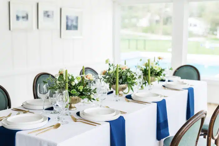 A rectangular table set up for an event with pink and white flower centerpieces running down the middle with long green candles on wither side of the flower arrangements.