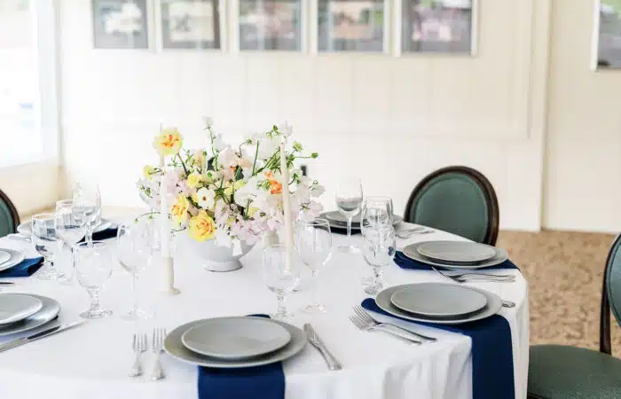 A close up of a round table with a yellow and pink flower centerpiece set up for a wedding.