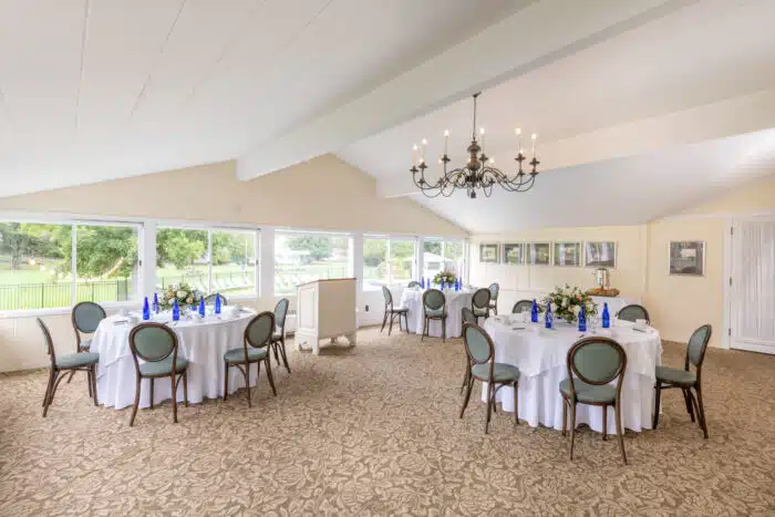 Several round tables with white table clothes set up for an event with flower centerpieces.
