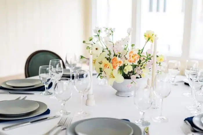 A close up of a round table with a yellow and pink flower centerpiece set up for a wedding.