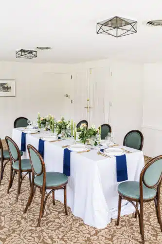 A rectangular table set up for an event with pink and white flower centerpieces running down the middle with long green candles on wither side of the flower arrangements.