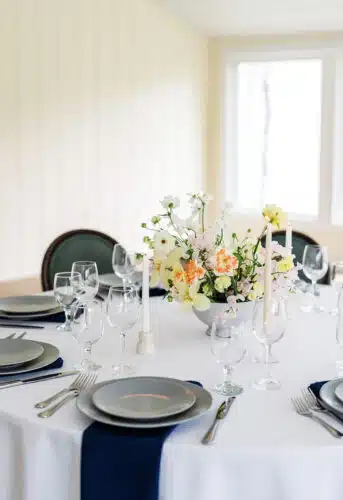 A close up of a round table with a yellow and pink flower centerpiece set up for a wedding.