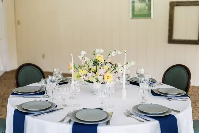 A close up of a round table with a yellow and pink flower centerpiece set up for a wedding.