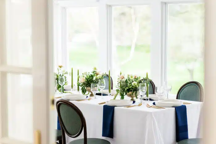 A rectangular table set up for an event with pink and white flower centerpieces running down the middle with long green candles on wither side of the flower arrangements.