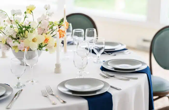 A close up of a round table with a yellow and pink flower centerpiece set up for a wedding.