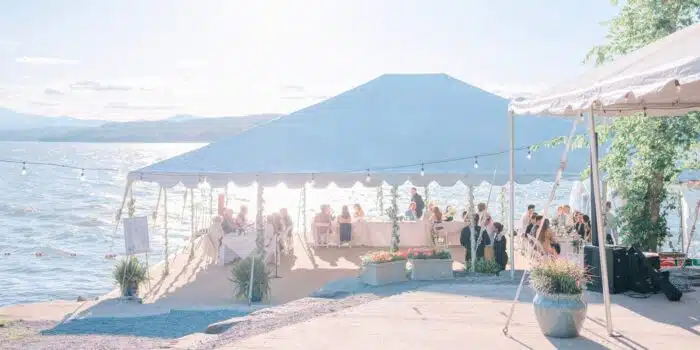 A wedding reception under a big white tent on the docks next to the lake.
