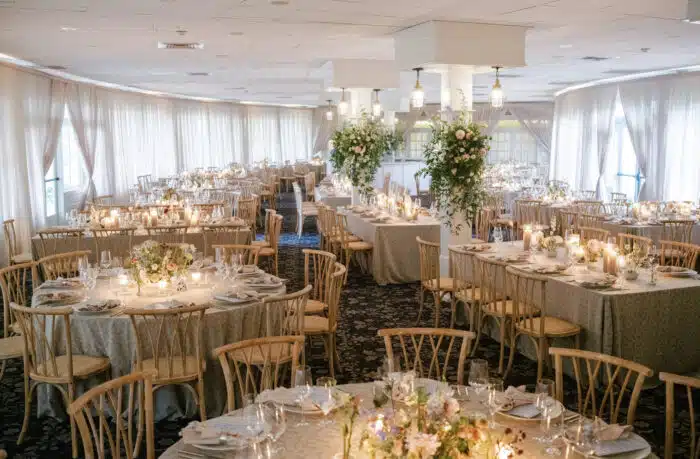 The main dining room decorated for a wedding with floral arrangements attached to the four floor to ceiling pillars. The dining tables are draped in a white and gold tablecloth.
