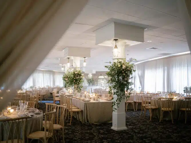 The main dining room decorated for a wedding with floral arrangements attached to the four floor to ceiling pillars. The dining tables are draped in a white and gold tablecloth.