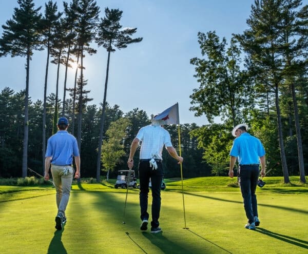 Three men finishing a put on the golf course